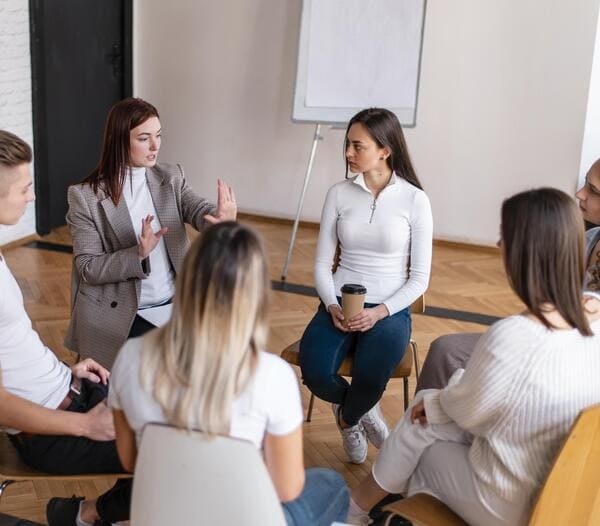 Séance de sophrologie collective avec 5 personnes assises en cercle et la sophrologue qui montrent les mouvements.